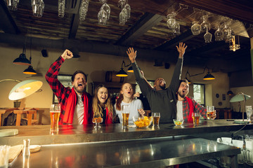 Wall Mural - Sport fans cheering at bar, pub and drinking beer while championship, competition is going. Multiethnic group of friends excited watching translation. Human emotions, expression, supporting concept.