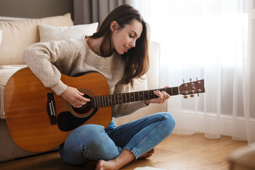 Image of happy beautiful woman playing guitar and composing song