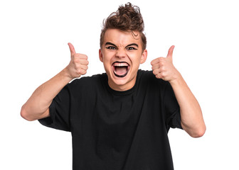 Poster - Portrait of teen boy with spooking make-up thumbs up gesture, isolated on white background. Caucasian young teenager in style of punk goth dressed in black screaming and showing success sign.