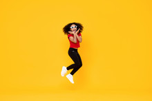 Happy Fashionable African American Girl Jumping In Mid-air With Hands On Chin Isolated On Yellow Background