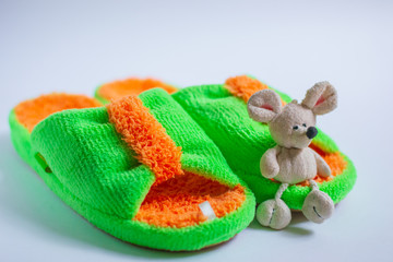 A toy mouse sits on bright fluffy slippers, isolated on a white background. Home women's or children's clothing. The concept of home warmth and comfort. Selective focus.