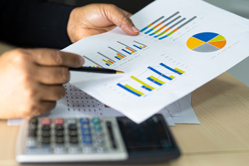 Asian accountant working and analyzing financial reports project accounting with chart graph and calculator in modern office : finance and business concept.