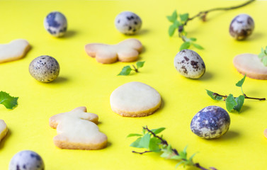 Easter composition with cookies, quail eggs and birch tree branch with fresh leaves on yellow paper background. Easter symbols and traditions. Butter and sugar cookies.