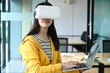 © sarawutnirothon - Cropped shot of a young female student wearing a VR glasses and using a laptop.