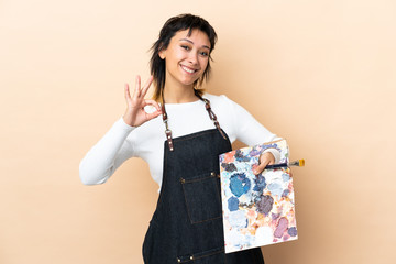 Wall Mural - Young artist man holding a palette over isolated background showing an ok sign with fingers