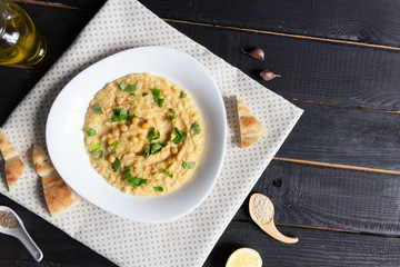 Canvas Print - Hummus plate, its ingredients, bread  on textile cover on black  background 