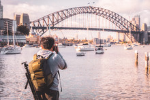 Traveller Man Young Backpacker Standing And Using A Professional Mirrorless DSLR Camera Take Photo Beautiful Of Sydney City Skyline With Sydney Harbour Bridge North Shore In Australia.