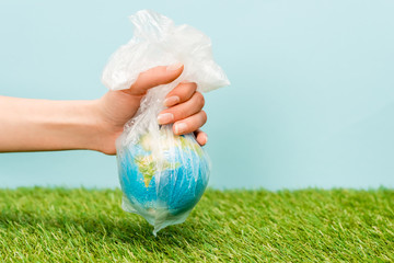 Wall Mural - Cropped view of woman holding plastic bag with globe on green and blue, global warming concept