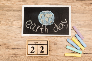 Wall Mural - Top view of board with earth day lettering, pieces of chalk and calendar with 22 april inscription on wooden background