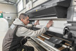 © guruXOX - Technician operator changes paper roll on large printer plotter machine