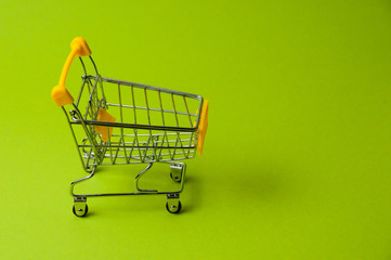 Wall Mural - Trolley for shopping on a green background. Supermarket food price concept, holiday discounts