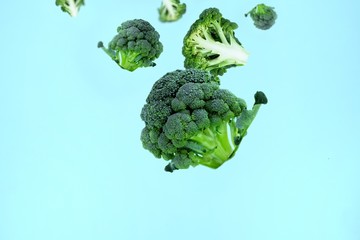 Flying green broccoli slices on a blue background. Concept of flying food, green vegetables, diet food, veggies pattern. Copy space for text.