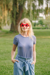 Wall Mural - Beautiful blonde Caucasian young girl wearing canadian maple leaf sunglasses. Happy woman with funny red glasses. Citizen female celebrating Canada Day on July 1 outdoors.