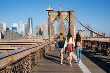 Three Girls Walking On The Brooklyn Bridge With The New York Skyline On The Back