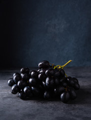 a cluster of juicy black grapes lies  on a dark gray table