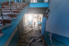 Lonely Person On Background Of Broken Stairwell And Entrance To Abandoned Old Hospital