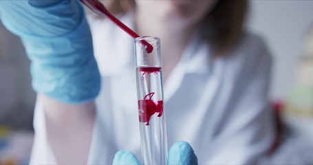 Wall Mural - Scientist with pipette analyzes red colored liquid to extract the DNA and molecules in the test tubes.