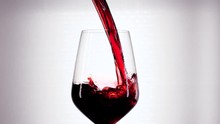 Slow Motion Of Pouring Red Wine From Bottle Into Goblet. Close-up Of Red Wine Forms Beautiful Wave In Glass. Wine Pouring In Glass At White Background.
