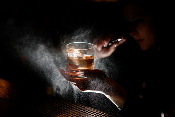 Bartender holds in one hand glass with alcoholic drink and sprinkles on it.