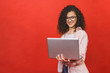 © denis_vermenko - Portrait of an excited curly young girl holding laptop computer isolated over red background.