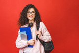 Fototapeta  - Young curly student woman wearing backpack glasses holding books and tablet over isolated red background.