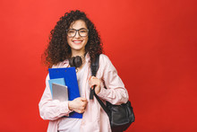 Young Curly Student Woman Wearing Backpack Glasses Holding Books And Tablet Over Isolated Red Background.