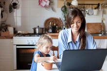 Working Mom Works From Home Office With Kid. Happy Mother And Daughter. Woman And Cute Child Using Laptop. Freelancer Workplace In Cozy Kitchen. Female Business, Career. Lifestyle Family Moment.