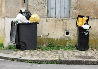 Two dark grey waste bins recycled bins filled with garbage and plastic bags