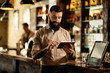 Smiling barista using digital tablet while working in a bar.