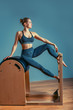 © Georgii - Young girl doing pilates exercises with a reformer bed. Beautiful slim fitness trainer on reformer gray background, low key, art light. Fitness concept