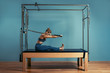 © Georgii - Young girl doing pilates exercises with a reformer bed. Beautiful slim fitness trainer on reformer gray background, low key, art light. Fitness concept