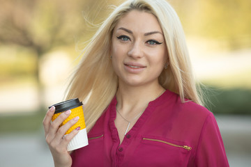 Wall Mural - Cheerful fashionable blonde holding coffee outdoors.Young woman drinking coffee on the street of the city.