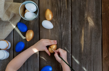 Wall Mural - Happy Easter.Kids paints with paint balls and wooden crafts.Blue, Golden eggs on a rustic wooden background on a Sunny day.Spring holiday.DIY.Instructions. Preparing for the holiday.Flat lay