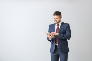 Wall Mural - Handsome businessman with tablet computer on light background