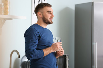 Wall Mural - Young man drinking water in kitchen