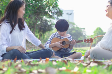 Poster - Happy Asian family has leisure in the park on the weekend or holiday. Mother teach son to play guitar. Grandmother enjoy this beautiful moment of love. Family generation relationship or bonding photo