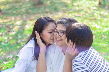 Poster - Asian lovely young daughter and grandson kiss happy and healthly senior woman or pleasure grandmother in moment of beautiful love in the park. Family generation relationship or bonding photo concept