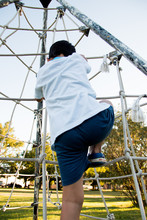 Rear View Of Boy Climbing On Jungle Gym At Playground