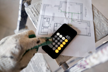 The construction worker calculates the area of the room on the calculator. Architectural blueprints. Repair or construction of a new apartment. Development of the apartment project.