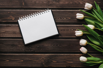 Wall Mural - White tulips on a wooden table with an empty notebook. Flat lay, top view composition