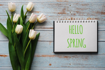 Wall Mural - Bouquet of white flowers of tulips on the background of blue boards with a notebook with lettering Hello Spring