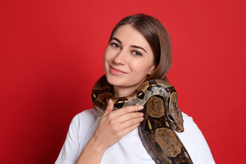 Canvas Print - Young woman with boa constrictor on red background. Exotic pet