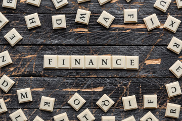 Wall Mural - Finance word made of square letter word on wooden background, random letters around.