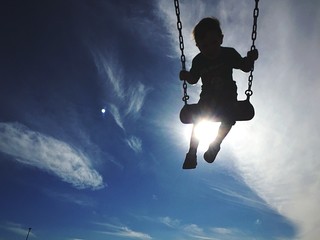 silhouette boy on swing against sky