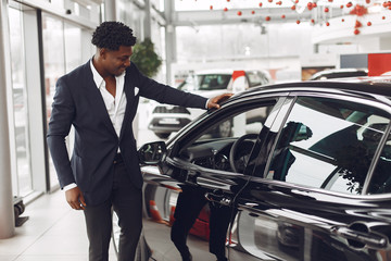 Man buying the car. Businessman in a car salon. Black male in a suit.