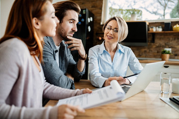 Wall Mural - Smiling financial advisor using laptop while having a meeting with young couple.