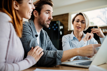 Wall Mural - Young couple using laptop with their financial advisor while having a meeting at home.