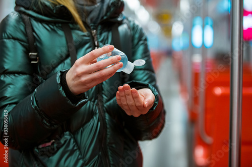 Woman in winter coat with protective mask on face standing in subway car, using hand sanitizer, looking worried. Preventive measures in public places of epidemic regions. Finland, Espoo