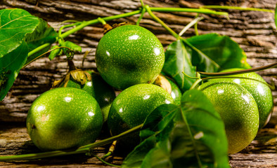 Fruits of green passion fruit (Passiflora edulis Sims) between leaves on wooden background