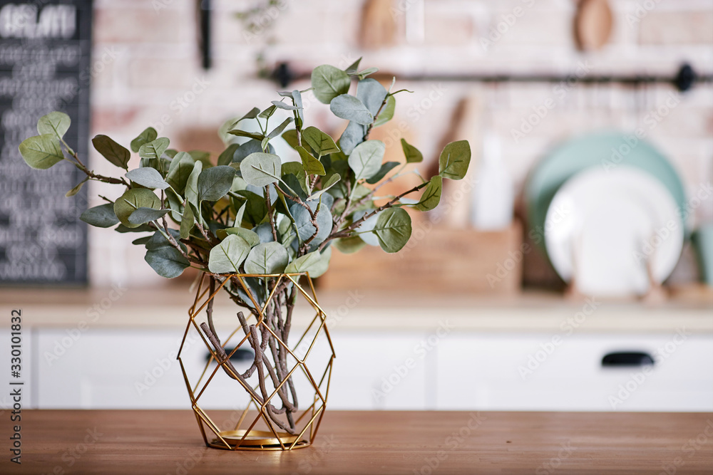 Metallic geometric decorative through vase with artificial eucalyptus branches on a wooden table. - obrazy, fototapety, plakaty 